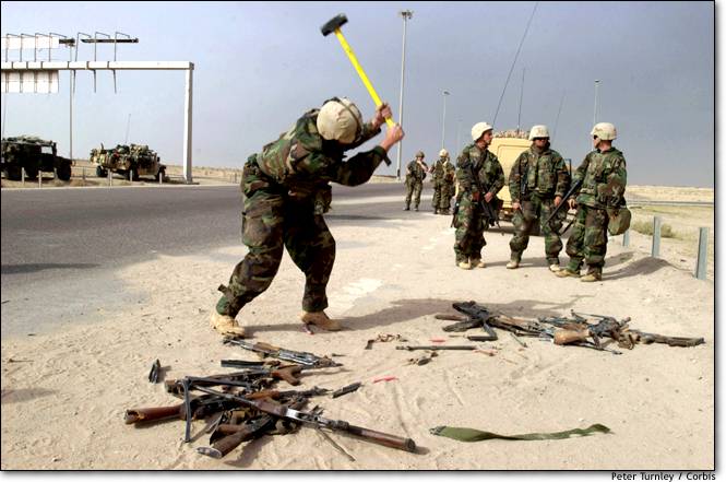 Soldiers in Iraq destroying guns and weapons by smashing them with a sledge hammer.
